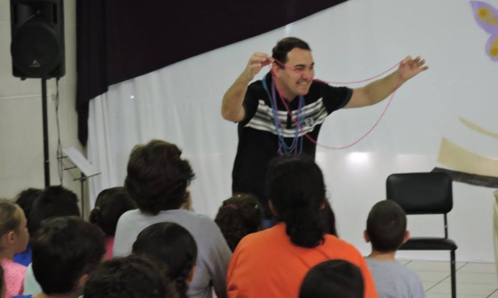 Carlos G. Steigleder durante uma contação de histórias diante de estudantes vistos de costas.